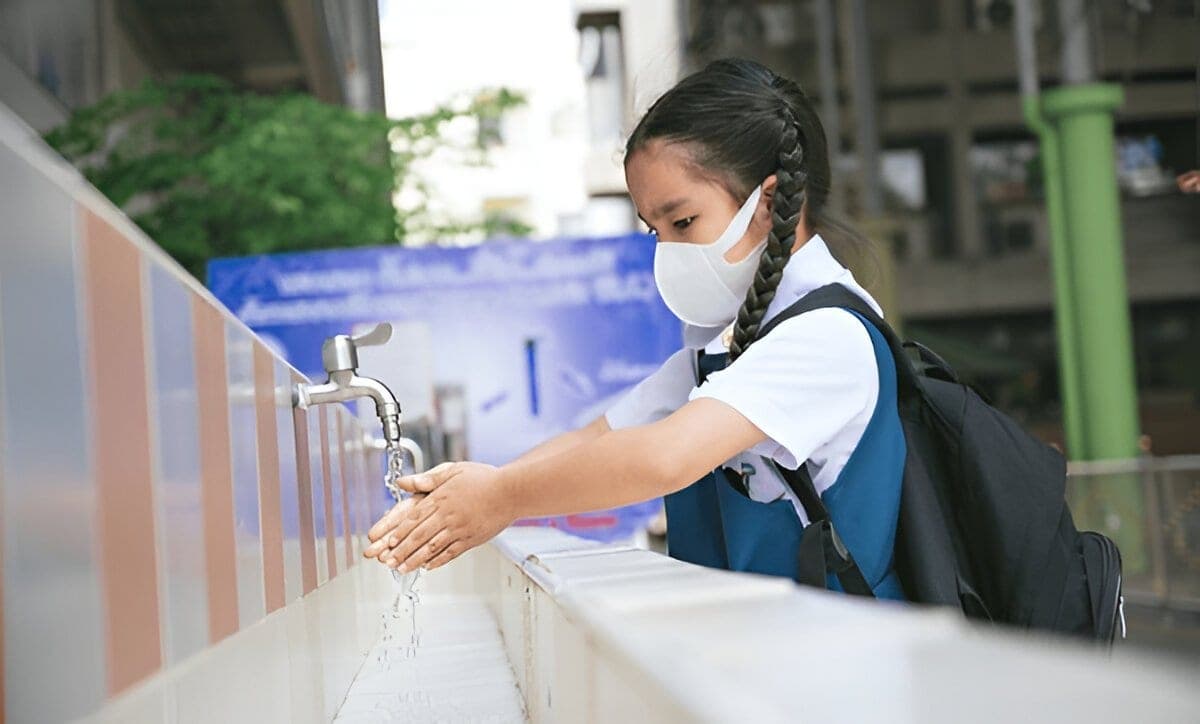 A school pupil washing their hands at an outdoor tap.