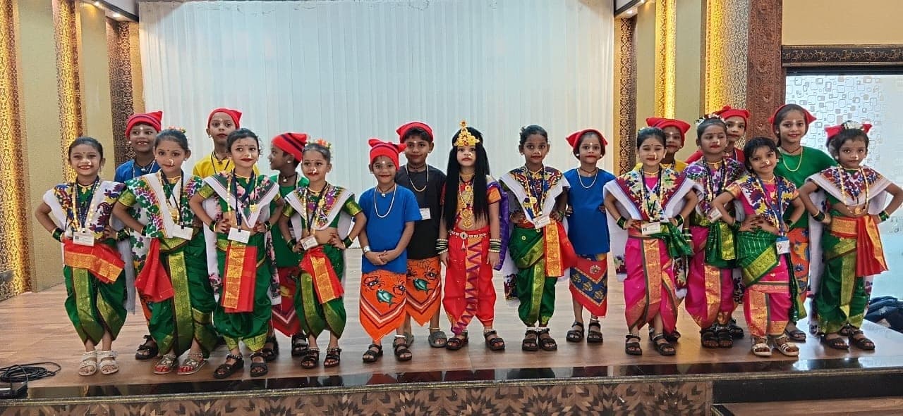 A long line of Kindergarten children in green and pink Maharashtrian costume standing across a stage at the end of a performance.