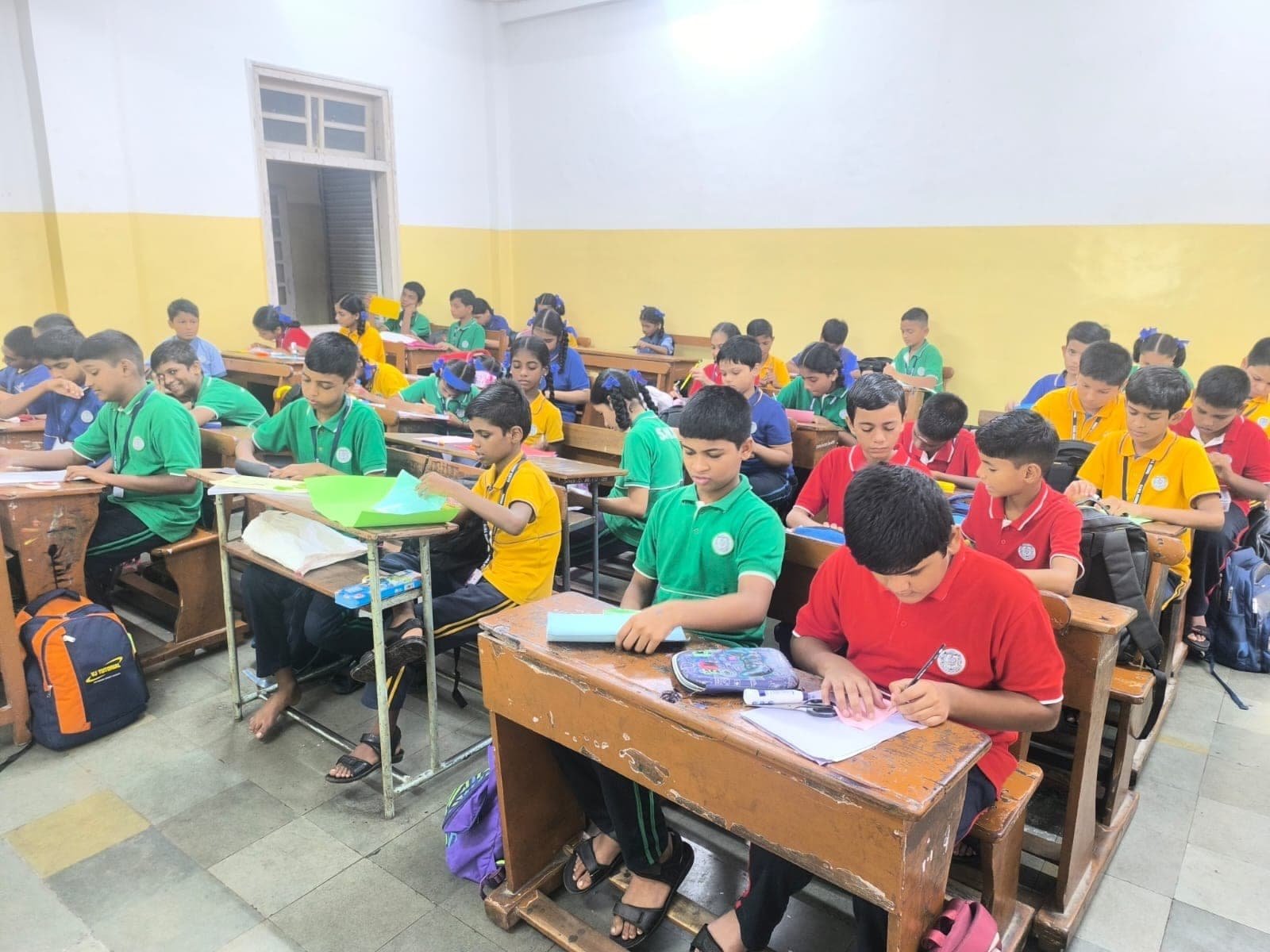 Secondary students at their desks during an activity session, writing and cutting coloured paper.