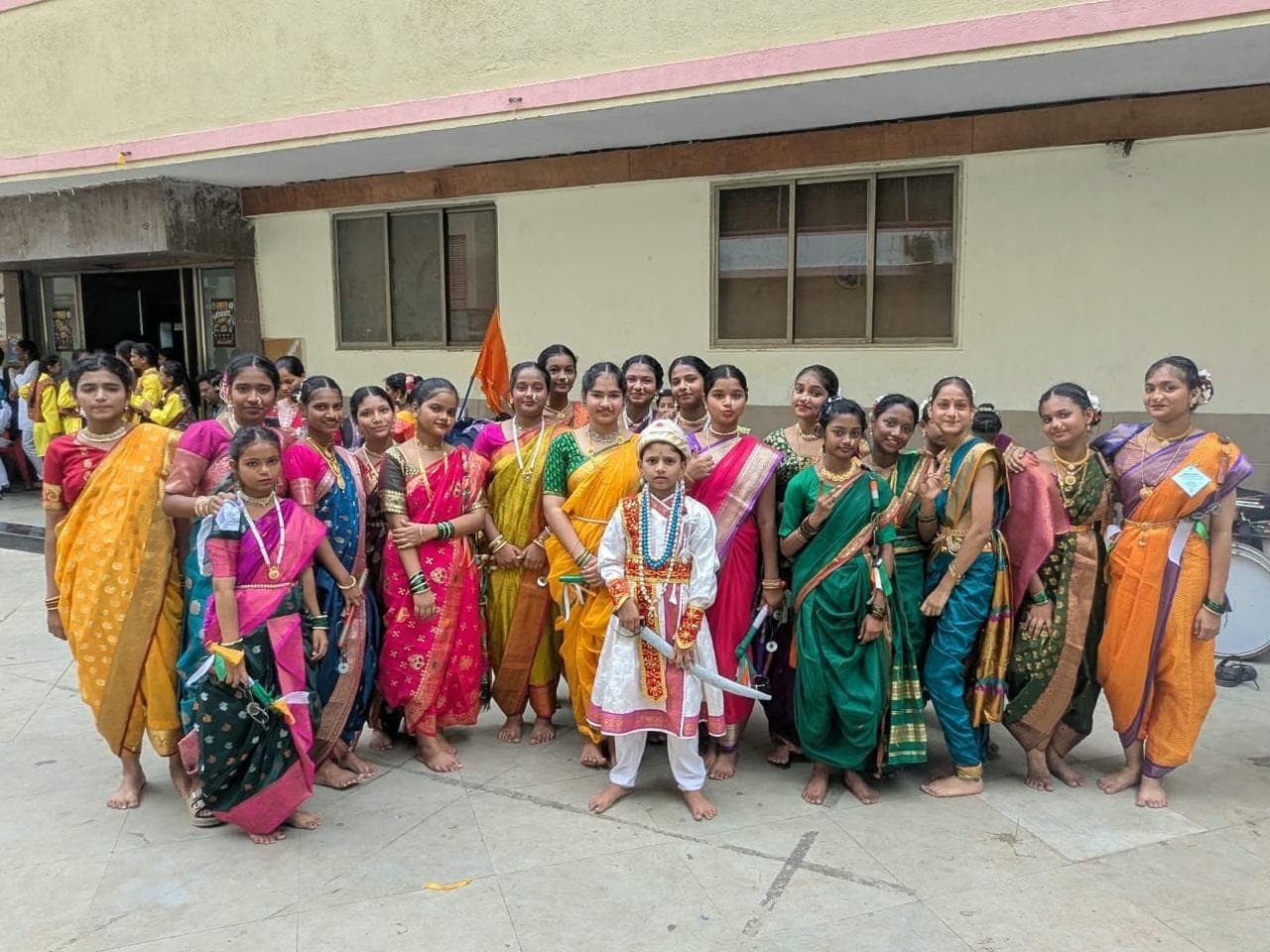 Secondary students in traditional Maharashtrian dress on the school ground, one in costume with a sword.