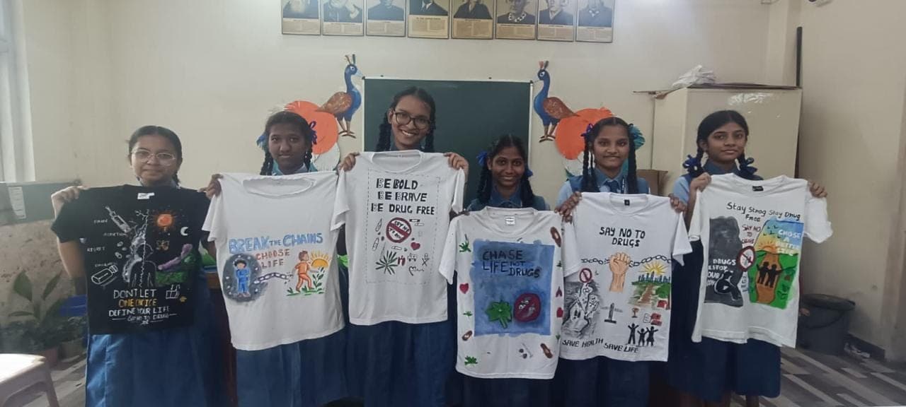 Secondary girls holding T-shirts they painted with anti-drug slogans and artwork.