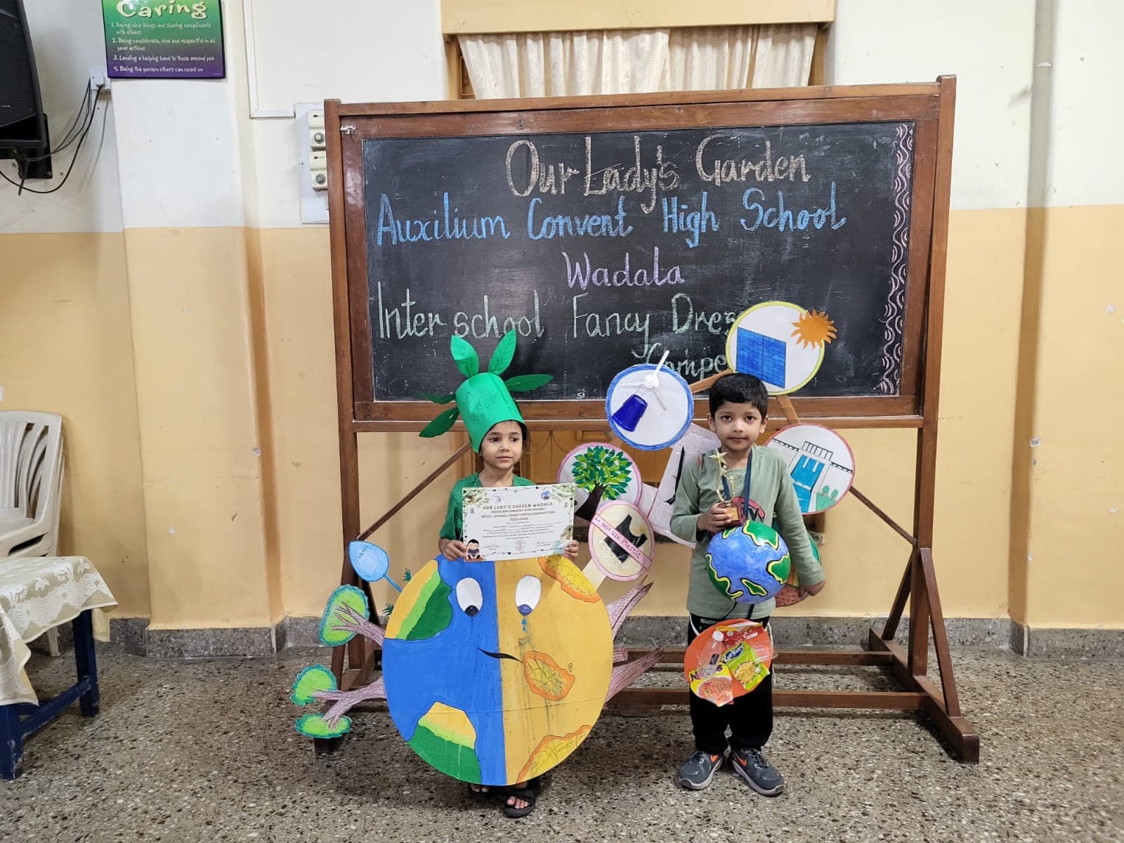Two young students in a fancy-dress competition, one wearing a painted globe costume and the other holding a model of the Earth.