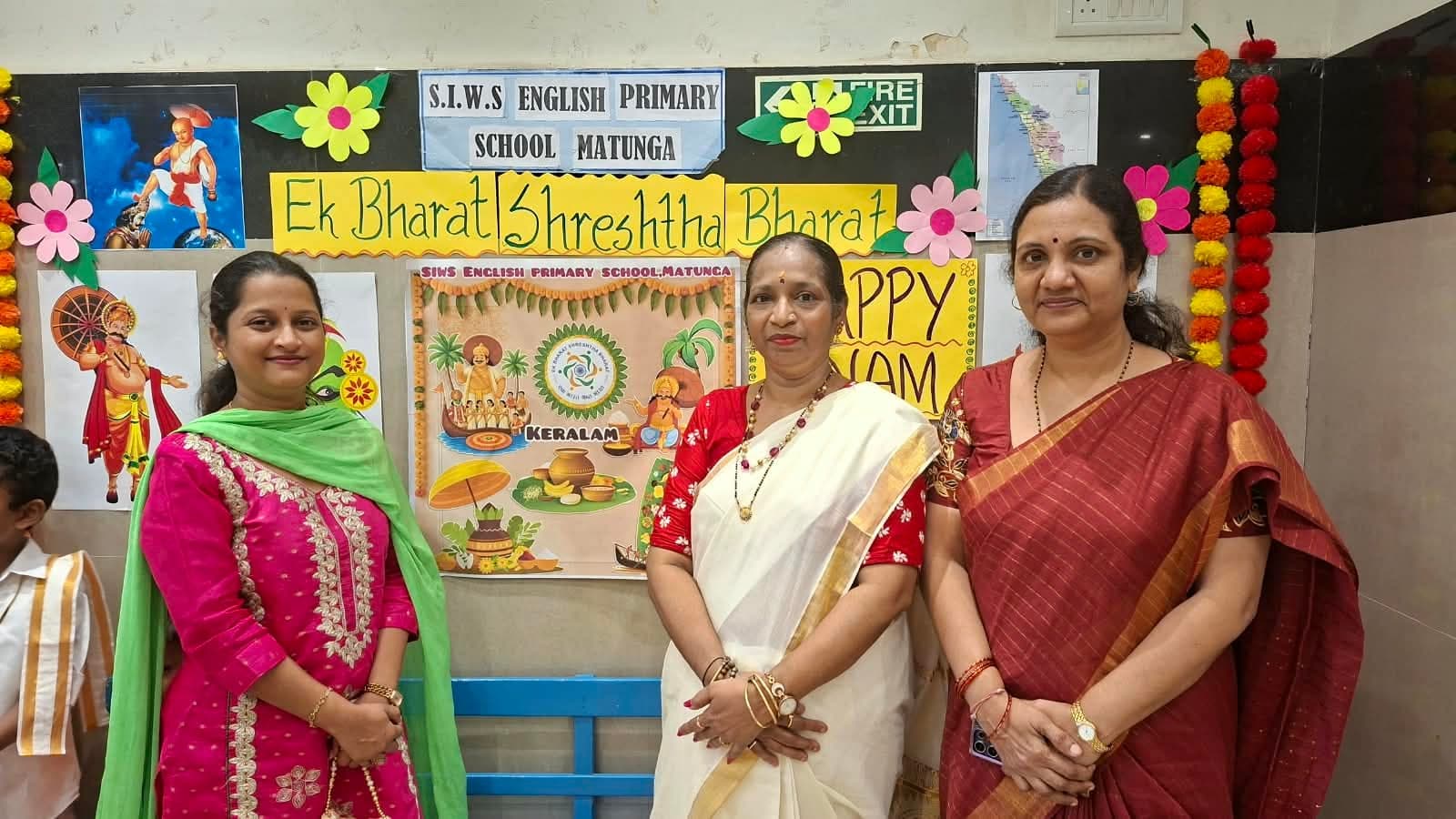 Three members of staff standing in front of the classroom display board reading “Ek Bharat Shreshtha Bharat” and “Keralam”, decorated with marigold garlands and illustrations of King Mahabali.